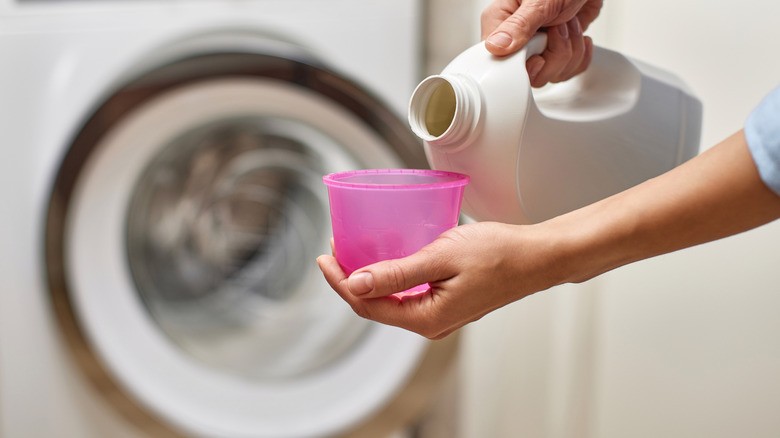 A person pouring bleach into a pink cup to clean the washing machine.