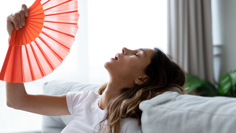 woman looking hot, leaning backward on a white couch, fanning herself with an orange fan
