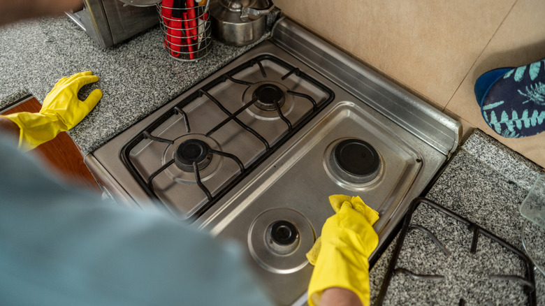 gloved person cleaning greasy stove top with sponge