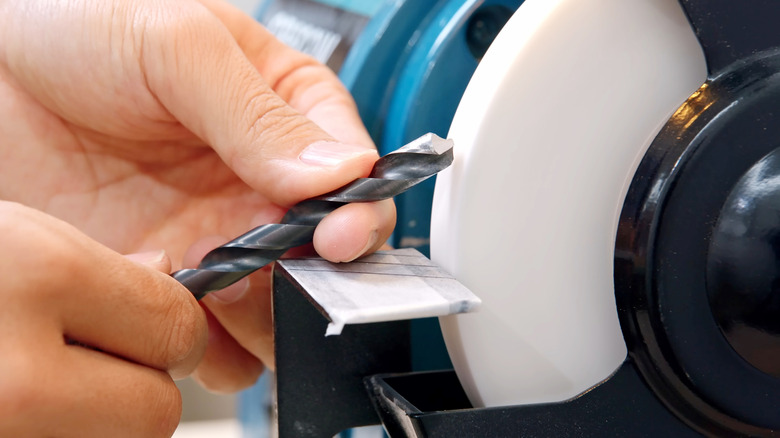 a person holding a drill bit next to a bench grinder
