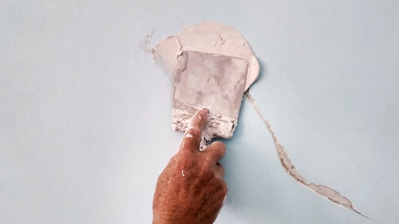 Image of a hand patching a crack in a wall.
