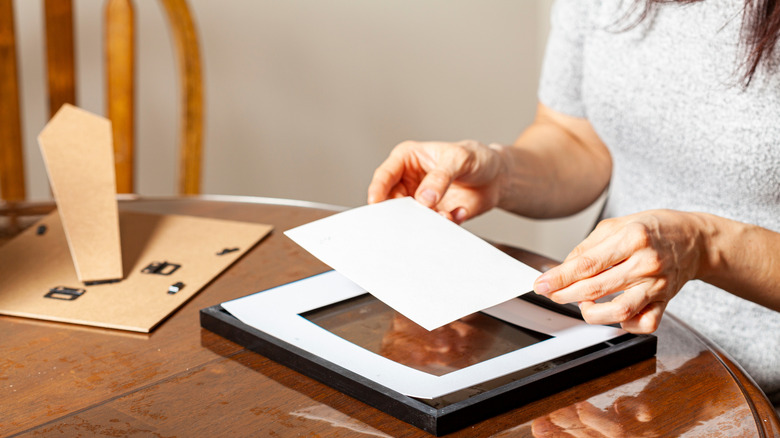 Person placing a photogram in a frame at kitchen table
