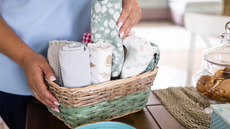 A person putting small towels in a wicker basket in kitchen