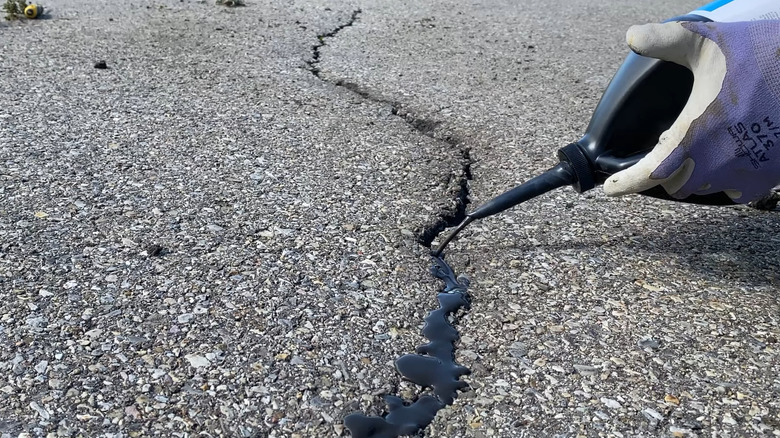 Person applying an asphalt crack filler with gloved hands