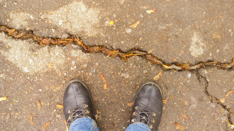 Closeup of a man's shoes standing on a cracked asphalt driveway