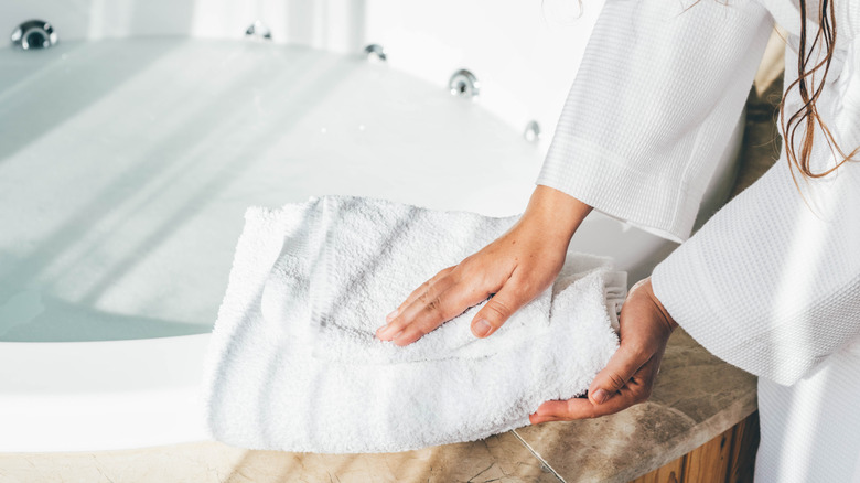 Woman placing white towels on edge of bath tub.