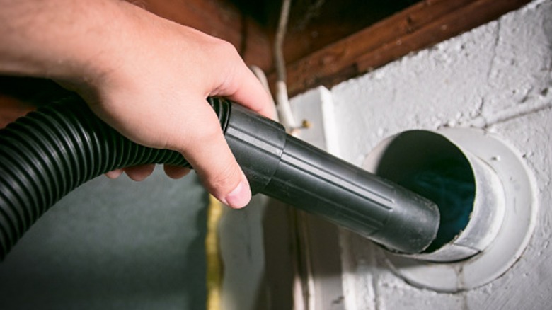 Person vacuuming inside a duct opening