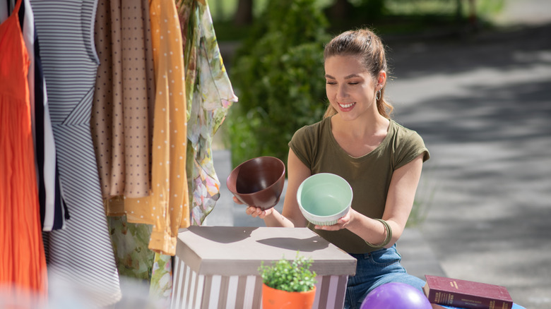 A woman smiles as she holds up brown and blue mixing bowls at a vintage market