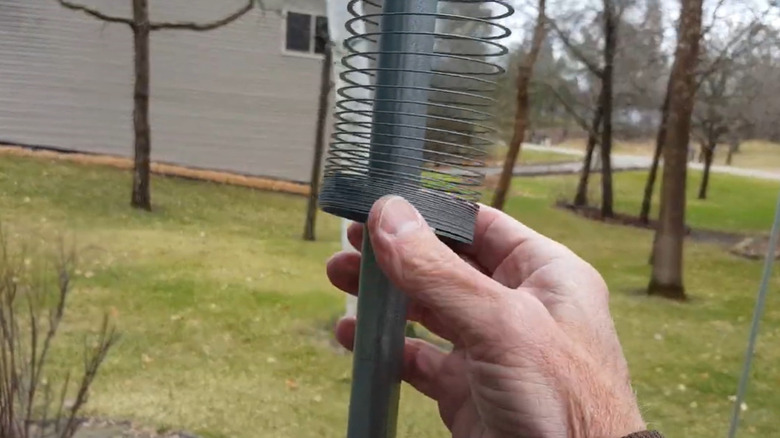 A man's hand pulling a Slinky toy down around a bird feeder pole.