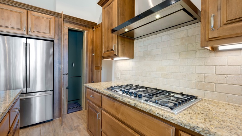 Honey oak cabinets in kitchen with white tile walls and wood flooring