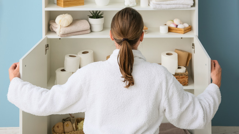 A woman looking through a bathroom cabinet