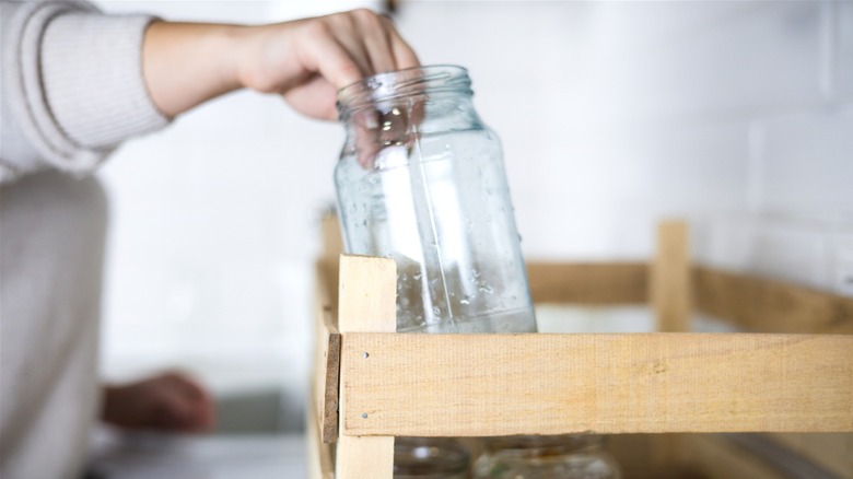 Person in kitchen pulling a clean Mason jar from a crate