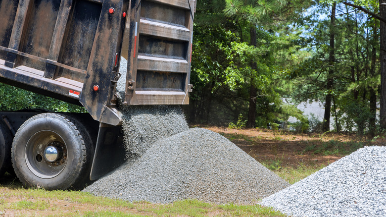 A truck unloading large quantities of gravel in a grassy yard.