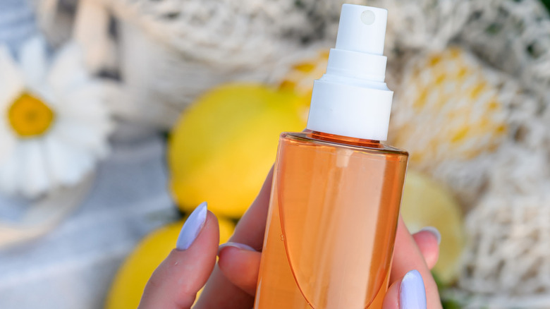A person holds a spray bottle in front of some lemons