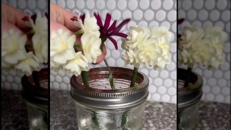 Colorful flower arrangement propped up in jar with mesh netting lid