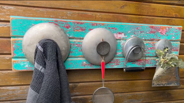 Mounted pot lids on a rustic farm door with large handles to hang objects on.