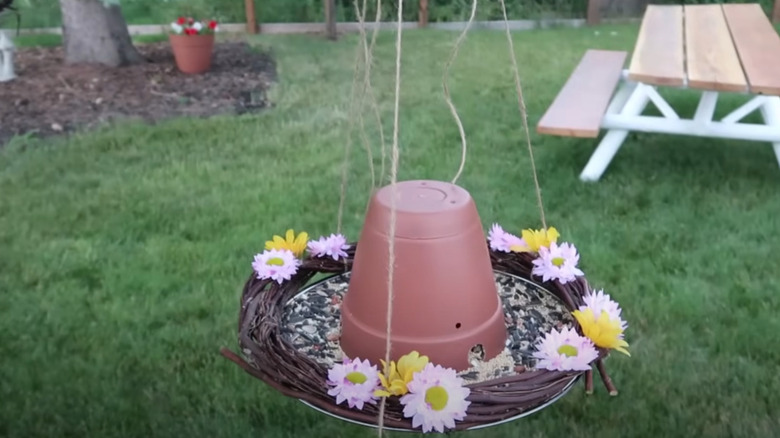 A bird feeder made from a terra cotta pot, a pot lid, a decorative wreath, and twine.
