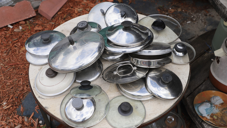 A pile of pot lids sitting on a table outside.