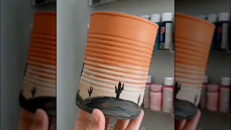 Woman holding up tin soup can with painted western scene