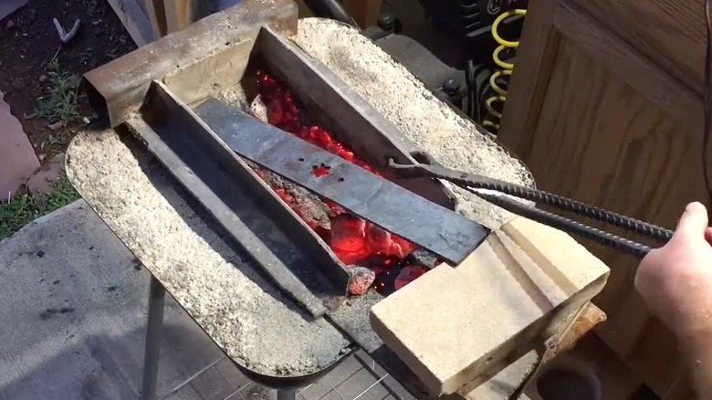 Person heating a lawn mower blade in a homemade forge