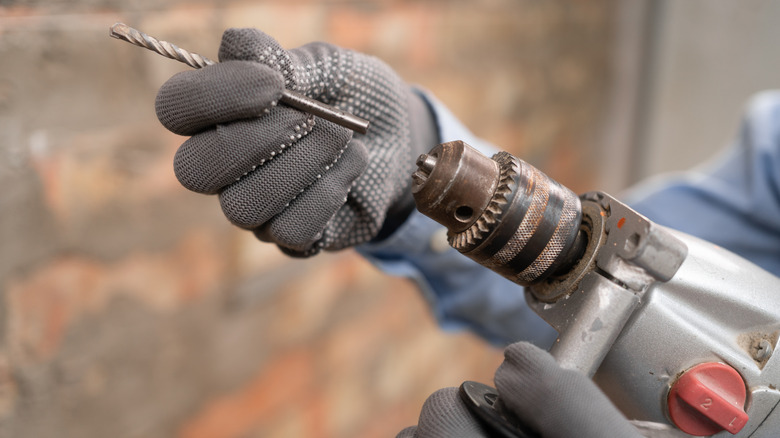 a gloved hand attaching a drill bit to a drill