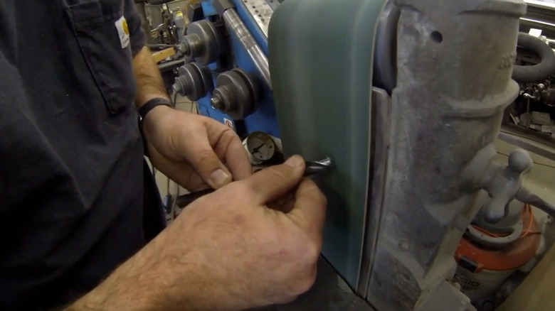 A man sharpening a drill bit on a belt sander