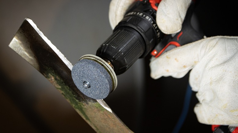 Person wearing gloves sharpens a blade with a drill attachment