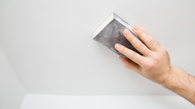 Person sanding a ceiling with a sanding sponge after covering texture