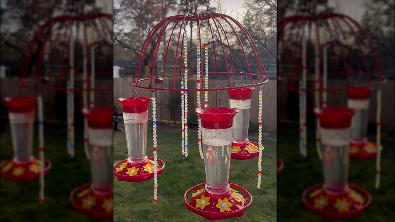 Three red hummingbird feeders hanging from an upside down planter painted red with strands of beads hanging down