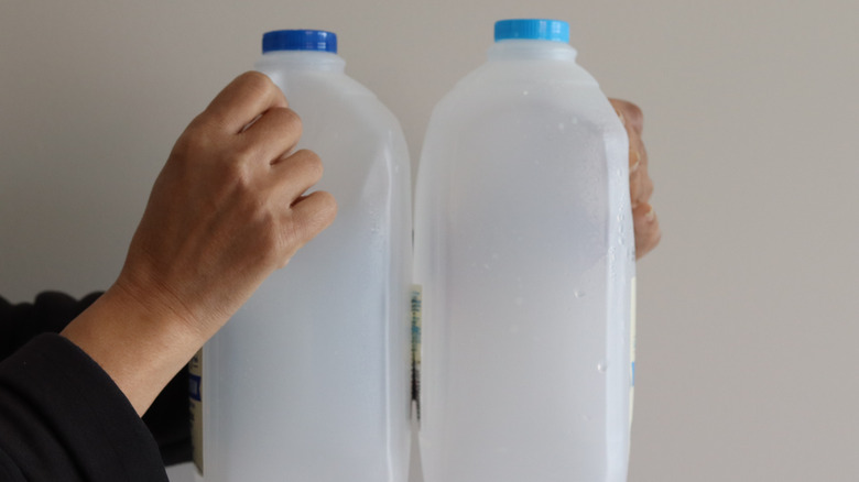 A person's hands holding two empty milk jugs