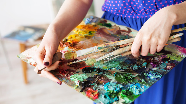 A woman in a blue polka dot dress holds a collection of paintbrushes with crusted paint