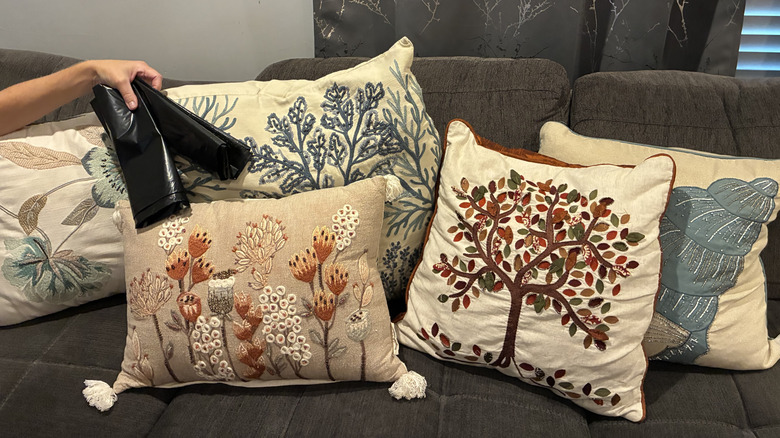 Couch full of throw pillows and person holding garbage bags for hack
