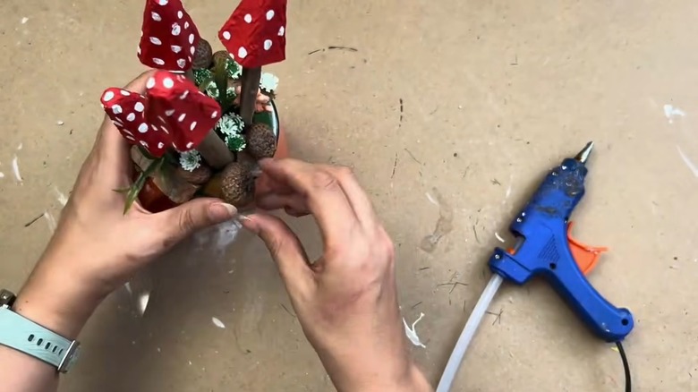 Female hands gluing an acorn to a whimsical mushroom village