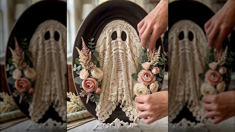 Person attaching faux flowers to a fall decor piece with a doily ghost mounted on a picture frame