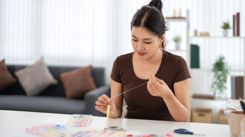 A woman stringing beads in her home to make a windchime.