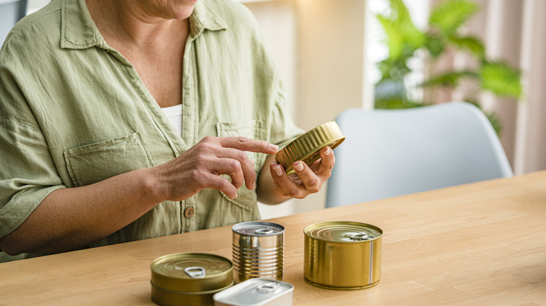 Person examines assortment of tin cans on a table.