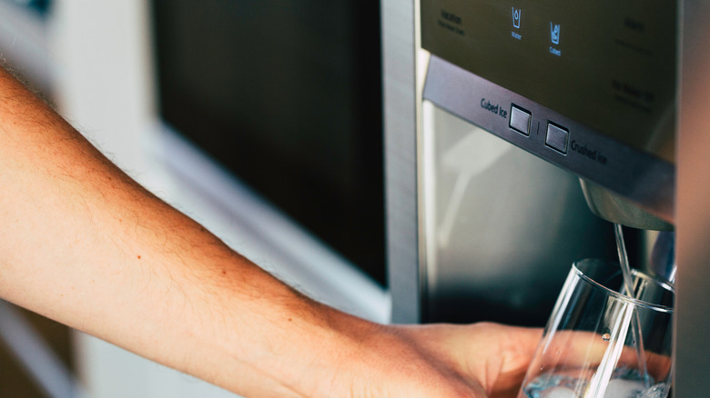 person filling a glass of water from their fridge