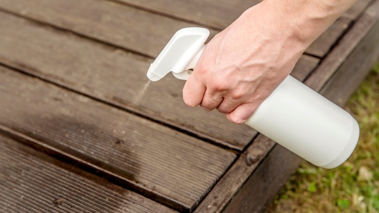 man spraying his outdoor deck with a spray bottle