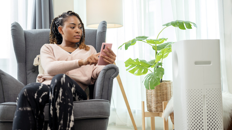 A woman sitting in a chair with a phone n her hand and a humidifier in the foreground