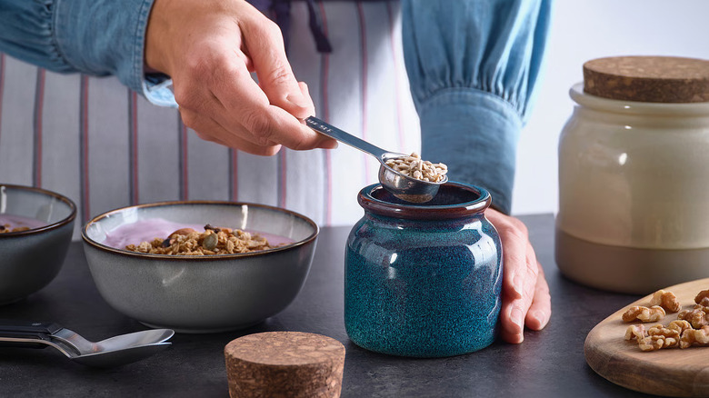 a woman spoons grains into a BRUGDHAJ Jar from IKEA