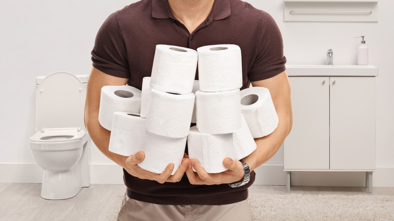 A man holds piles of toilet paper rolls