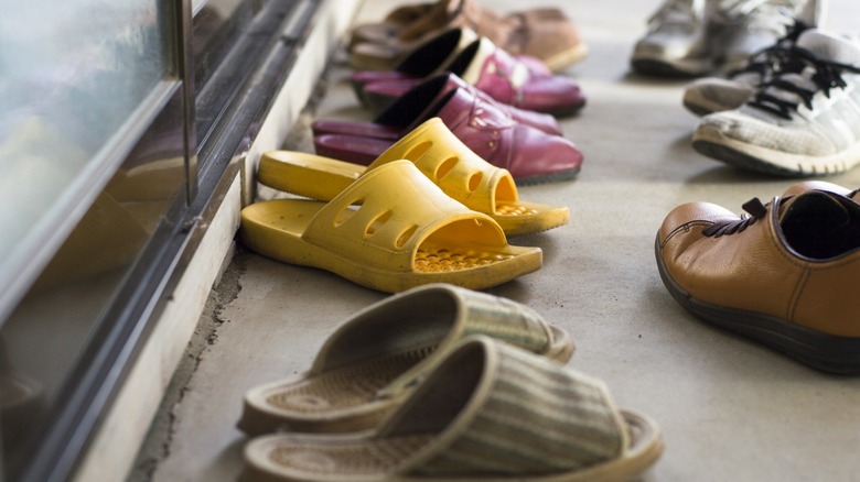 Pairs of slides and shoes on concrete patio outside sliding glass door