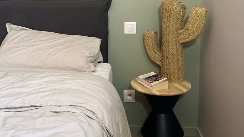 A DIY round side table with a book and faux cactus on it next to a bed