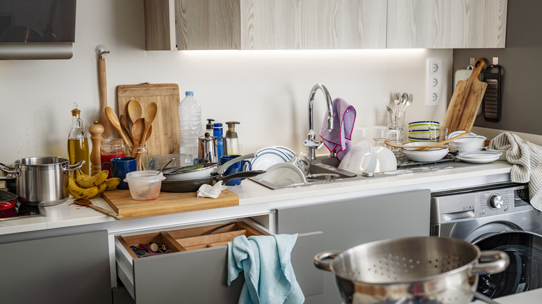 Kitchen countertop with lots of loose items and dishes on it