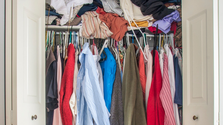 overstuffed closet with hanging garments on rod and extra clothes piled on the shelf above