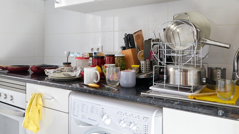 Countertops in a messy kitchen are covered in dishes and cooking items