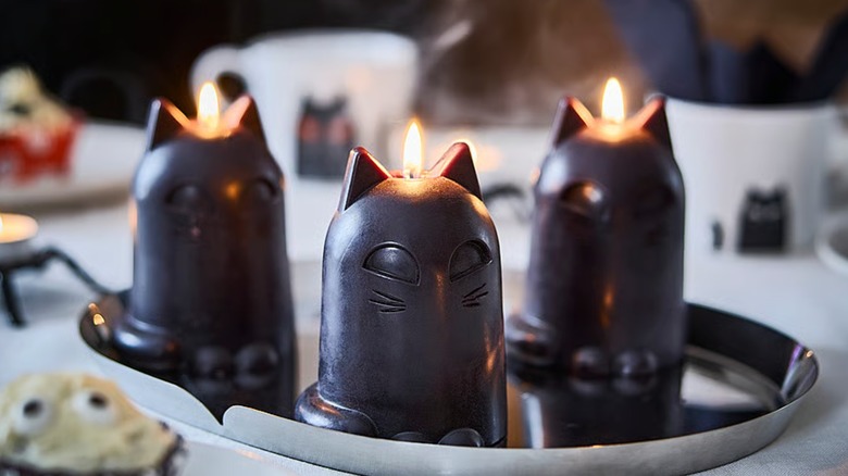 Three lit black cat-like candles on a steel dish