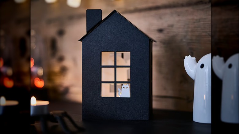 A cat figurine peeking out the window of a black house