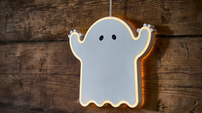 A lit LED ghost hanging against a wood surface