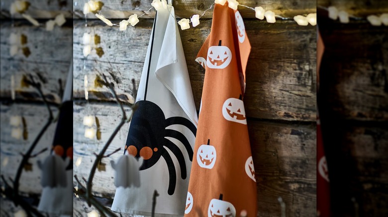 A white and an orange Halloween-themed dish towel hanging from hooks